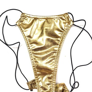 May include: Gold metallic bikini bottom with adjustable straps. The front of the bikini bottom is shown. The bikini bottom is made of a shiny, metallic fabric.
