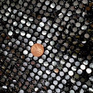 Puede incluir: Tela negra con lentejuelas plateadas en un patrón de lunares. Un centavo de cobre se coloca sobre la tela.