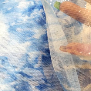 May include: Blue and white tie-dye fabric with a sheer, glittery overlay. The fabric is soft and delicate, and the glitter adds a touch of sparkle.