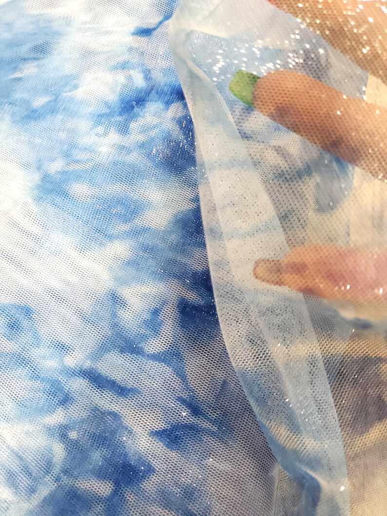 May include: Blue and white tie-dye fabric with a sheer, glittery overlay. The fabric is soft and delicate, and the glitter adds a touch of sparkle.