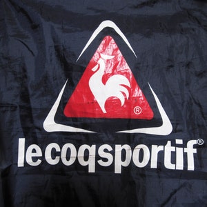 May include: A white rooster logo inside a red triangle with a white outline. The text "le coq sportif" is below the logo in white letters on a dark blue background.