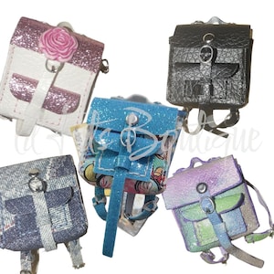 Puede incluir: Una colección de mini mochilas en varios colores y texturas. Las mochilas incluyen un diseño similar al denim, un rosa brillante con una rosa, un negro texturizado, un azul brillante y un acabado iridiscente pastel. Cada una tiene un cierre de hebilla y correas ajustables.