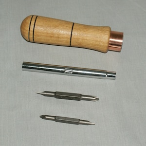 May include: A set of screwdriver bits with a wooden handle and a metal extension. The handle has a copper coloured end cap. The bits are silver and have a black tip.