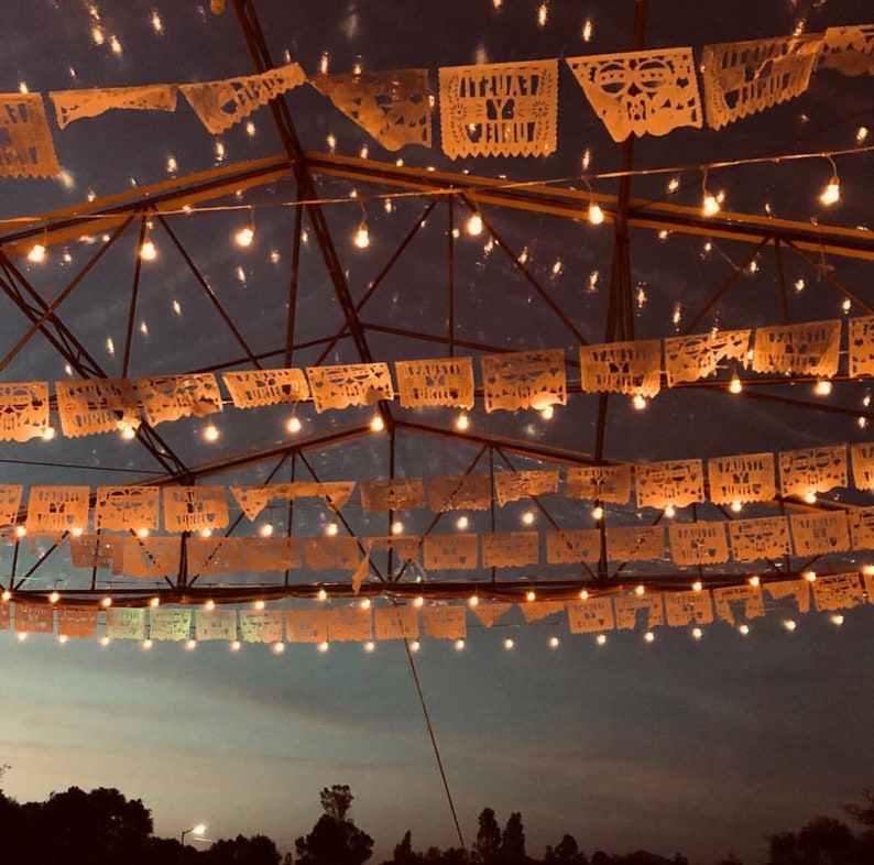 May include: A ceiling decorated with strings of white paper lanterns and white lights. The lanterns are shaped like triangles and squares.
