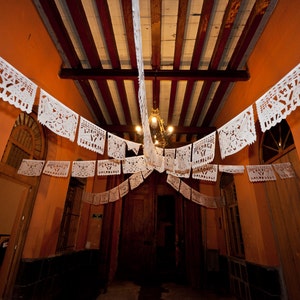 May include: An interior space decorated with white paper cutouts hanging from the ceiling. The cutouts are in the shape of flowers and leaves. The walls are painted a warm orange color.