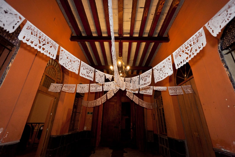 May include: An interior space decorated with white paper cutouts hanging from the ceiling. The cutouts are in the shape of flowers and leaves. The walls are painted a warm orange color.