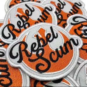 May include: Embroidered patches with the words "Rebel Scum" in black script. The patches feature a white and orange design with a circular shape. Suitable for jackets, bags, or other fabric items.