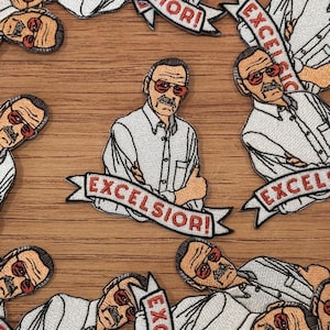 Può includere: Toppe ricamate raffiguranti un cartone animato di un uomo con occhiali da sole rossi e baffi, che indossa una camicia bianca. Le toppe hanno la scritta "EXCELSIOR!" su uno striscione. Le toppe sono sparse su una superficie di legno.