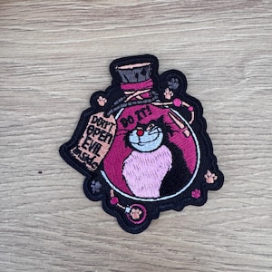 May include: Black and pink embroidered patch of a potion bottle with a black cat inside. The bottle has a tag that says "Don't open evil inside" and "Do it!"