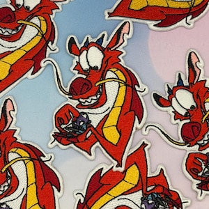 May include: Embroidered patches featuring a red dragon with yellow and white accents. The dragon is smiling and holding a small, purple object. The patches are on a colorful background, suitable for clothing or accessories.