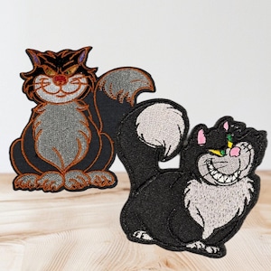 May include: Two embroidered patches of black cats with white fur. The cat on the left is sitting with its tail curled around its body. The cat on the right is lying down with its tail curled behind it. Both cats have green eyes and a mischievous grin.