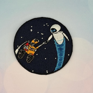 Puede incluir: Parche bordado circular que representa a WALL-E y EVE de la película animada. El parche tiene un fondo azul marino con estrellas blancas. WALL-E es amarillo y naranja, y EVE es blanco y azul. Los robots se tienden la mano.