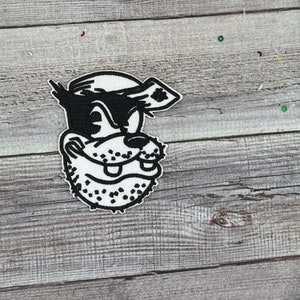 May include: Black and white embroidered patch of a cartoon dog wearing a sailor hat. The dog has a mischievous expression and is looking to the right.