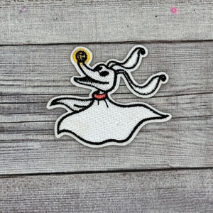 Könnte beinhalten: Weiß gestickter Patch eines Geisterhund-Charakters mit rotem Halsband und einer leuchtend gelben Kugel im Maul. Der Charakter stammt aus dem Film "Nightmare Before Christmas".