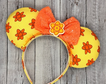 Op de afbeelding: Gele muisoren-hoofdband met oranje atoompatroonoren en een pailletten oranje strik. De hoofdband heeft een bijpassend atoompatroon en een kleine atoom-thema middenversiering. Een leuk accessoire.