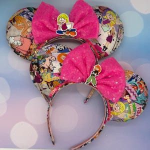May include: Pink sequined bow headbands with character decals. The ears are covered in a collage of images. One headband features a cartoon image of a girl sitting down, and the other features a cartoon image of a girl standing up.