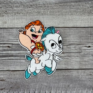 May include: An embroidered patch depicting a cartoon baby Hercules riding a winged white horse. Hercules is wearing a red and gold loincloth and holding a golden object. The horse has blue wings and a light blue mane.