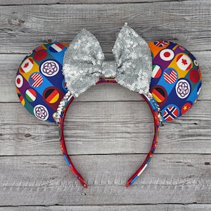 May include: A pair of red mouse ears with a silver sequin bow. The ears are covered in a fabric with a pattern of flags from around the world.