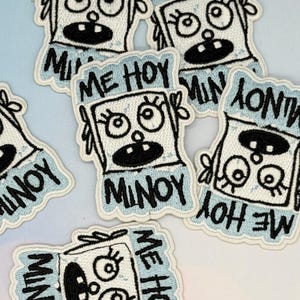 May include: Embroidered patches with a cartoon character design. The patches feature a white face with black eyes and mouth, surrounded by a light blue border. The text "ME HOY MINOY" is included in the design.