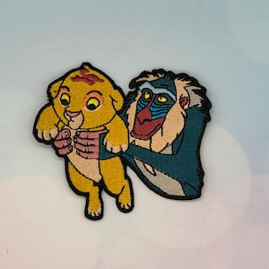 Puede incluir: Parche bordado con Simba de El Rey León, sostenido por Rafiki. Simba es amarillo con un mechón de pelo rojo, y Rafiki tiene una cara azul y beige con una capa verde azulado. El parche está diseñado para su aplicación en ropa o accesorios.