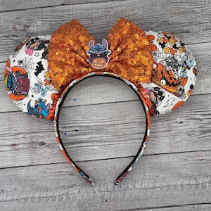 May include: Halloween-themed headband with orange sequin bow and character embellishment. The ears feature a white background with Halloween-themed characters and orange accents. The headband is black with orange and character details.
