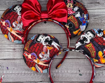 May include: Red fabric bow headband with two cartoon character themed fabric ear pieces. The ear pieces feature a red and white brick background with cartoon characters including Bugs Bunny, Jessica Rabbit, and Roger Rabbit. The text "Roger Rabbit" is printed on the ear pieces.