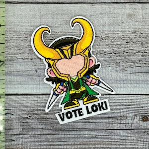 May include: An embroidered iron-on patch featuring a cartoon character of Loki from the Marvel universe. The character is wearing a green and gold costume with a horned helmet. The patch has the text "VOTE LOKI" on a white background.