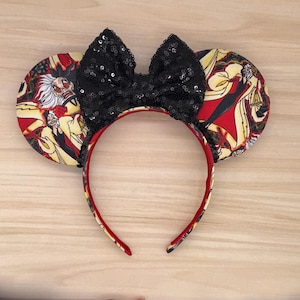 May include: A black sequined bow headband with two round ears. The ears feature a red, yellow, and black pattern with cartoon characters. The headband is red with a matching pattern on the inside.