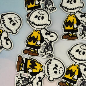May include: Embroidered patches featuring a cartoon character with a yellow shirt and black zig-zag design, and a white dog. The patches have a black outline and are on a light blue and white background.