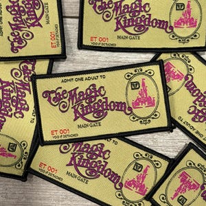 May include: A collection of rectangular patches with the text "The Magic Kingdom" in a stylized font. The patches are primarily tan with black borders and feature a pink castle illustration. Each patch includes the text "ET 001" and "Main Gate".