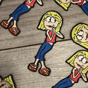 May include: Embroidered patches featuring a cartoon character in a red top, blue jeans, and orange shoes. The character has blonde hair and is in various poses. The patches are on a light gray wooden surface.