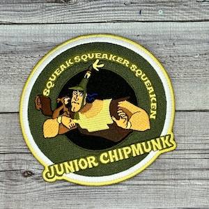 May include: A green and yellow embroidered patch with a cartoon image of a chipmunk and a man. The text "Squeak Squeaker Squeakin' Junior Chipmunk" is around the edge of the patch.