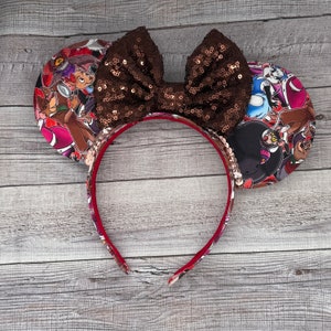 May include: Brown sequined bow headband with a red and brown fabric design featuring cartoon characters. The headband is made of red and brown fabric with a brown sequined bow.
