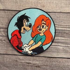 Op de afbeelding: Een ronde geborduurde patch met een cartoonhond en een cartoonmeisje. De hond draagt een rood jack en het meisje draagt een groen shirt. De patch heeft een lichtblauwe achtergrond.
