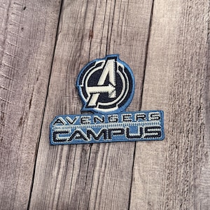 May include: A blue and white embroidered patch with the Avengers logo and the text "Avengers Campus".
