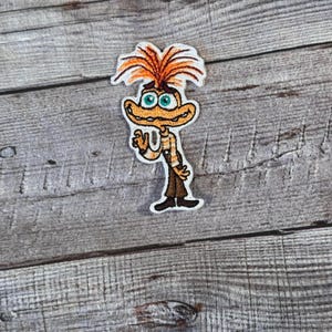 Puede incluir: Un parche bordado para planchar que presenta un personaje de dibujos animados con pelo naranja, ojos azules y una camisa a rayas marrones y blancas. El personaje está saludando con su mano derecha.