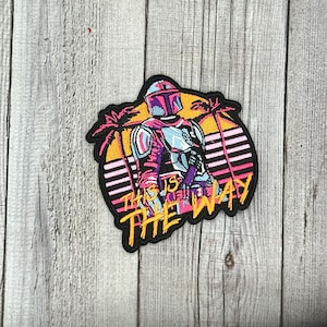 May include: A black and yellow embroidered patch featuring a retro-style illustration of a Mandalorian character with the text "This is the Way".