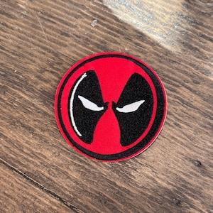 May include: Red and black embroidered patch featuring a stylised image of Deadpool's mask.