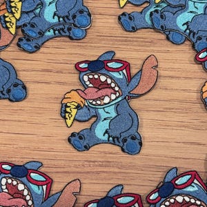 Könnte beinhalten: Blaue Stitch-Figur mit roten Sonnenbrillen, die ein Eiswaffel isst. Die Figur ist auf einem Stoffpatch gestickt.