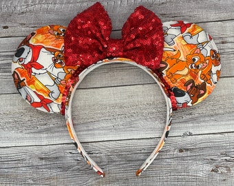 May include: Red sequined bow headband with a white fabric design featuring cartoon dogs and cats from the Disney movie The Aristocats.