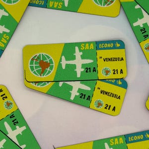 Pode incluir: Autocolantes retangulares verdes e amarelos com tema de viagem. Os autocolantes apresentam um gráfico de avião branco, o texto "SAA ECONO" e o destino "VENEZUELA". Os autocolantes também incluem um gráfico de globo e o número "21 A".