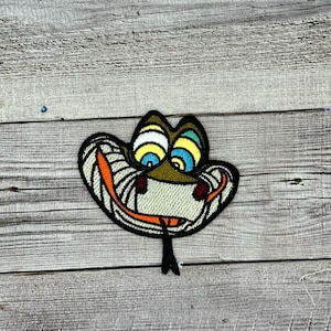 Op de afbeelding: Een groene slang met een brede, tandenrijke grijns en grote, kleurrijke ogen. De slang is geborduurd op een stoffen patch.