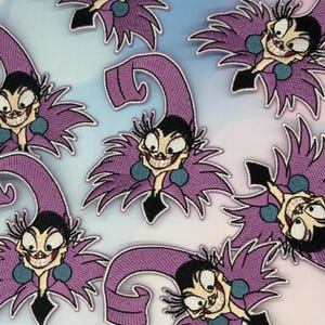 Può includere: Toppe ricamate raffiguranti un personaggio dei cartoni animati con un cappello e un colletto da giullare viola, un top nero e un ampio sorriso sdentato. Le toppe hanno una combinazione di colori viola chiaro, nero e verde acqua, con uno sfondo bianco.
