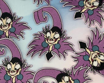 May include: Embroidered patches featuring a cartoon character with a purple jester hat and collar, a black top, and a wide, toothy grin. The patches have a light purple, black, and teal color scheme, with a white background.