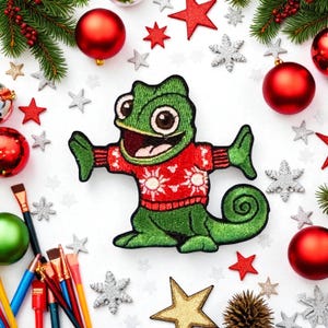 May include: Embroidered green chameleon patch wearing a red sweater with white snowflake designs. The patch is surrounded by Christmas ornaments, stars, and pine branches on a white background. A festive holiday decoration.