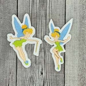 Könnte beinhalten: Zwei gestickte Bügelbilder mit Tinkerbell, einer Fee mit blonden Haaren, grünem Kleid, blauen Flügeln und einem Zauberstab.