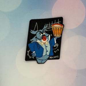 May include: A black embroidered patch featuring a blue owl character wearing a monocle, a light blue vest, and a gold bowtie. The owl holds an orange and white basket. White musical notes and the letters ABCDEFG are stitched on the black background.