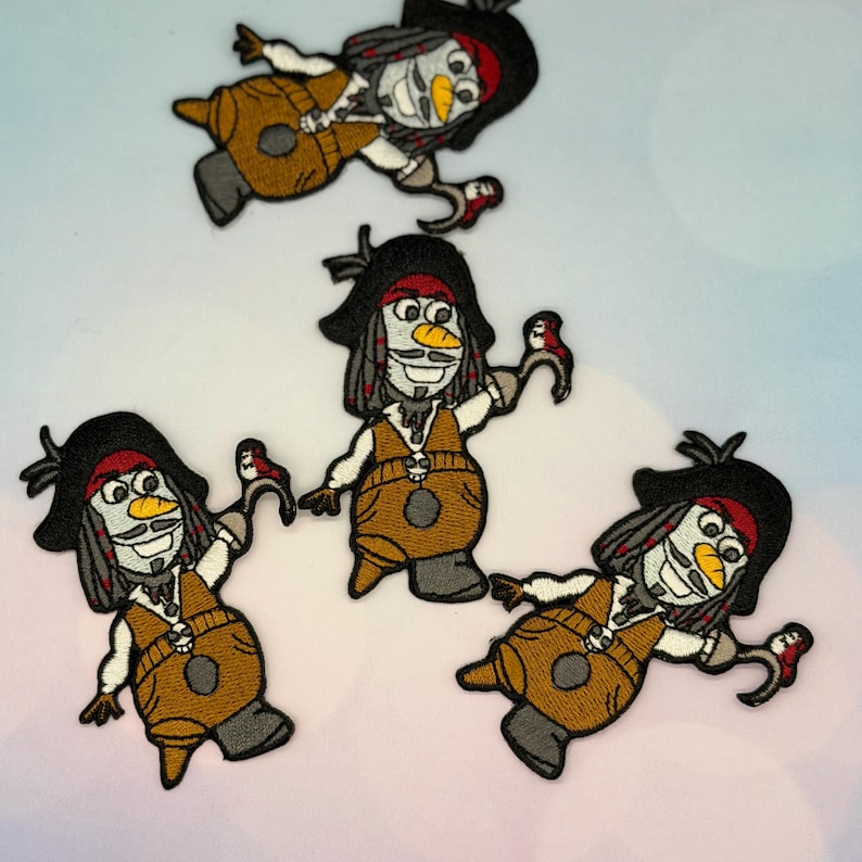 May include: Embroidered patches featuring a cartoon snowman dressed as a pirate. The patches have a black hat, red bandana, and brown vest. The snowman has a white face, gray hair, and a yellow beak. The patches are on a light blue background.