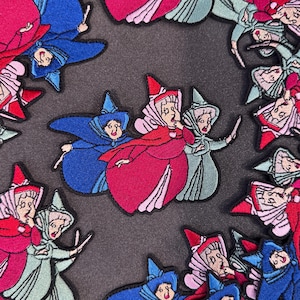 May include: Embroidered patches featuring three fairy characters in red, blue, and green robes and hats. The patches are in a repeating pattern, with the fairies in various poses. The patches are on a dark gray background.