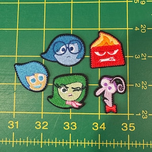 Puede incluir: Parches bordados con personajes de la película "Del revés". Los parches representan a Alegría, Tristeza, Ira, Asco y Miedo. Cada parche tiene un borde negro y está hecho con hilo colorido.